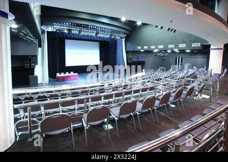 Postazione documenti sul palco e sul retro di file di sedie con corrimano nella grande sala per riunioni d'affari. Foto Stock