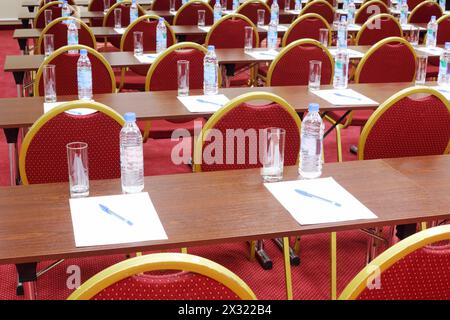 Retro di sedie rosse e tavoli in legno con bottiglie e bicchieri in una sala vuota per riunioni d'affari. Foto Stock