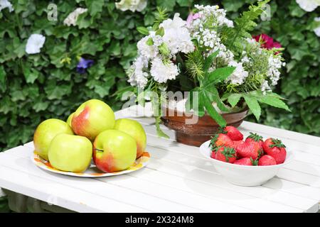 Piatti con mele, fragole e fiori su tavola bianca. Foto Stock