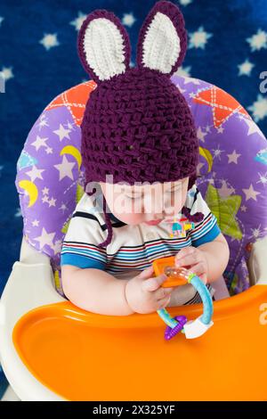 Un bambino con un cappello a maglia con orecchie di coniglio gioca con un giocattolo Foto Stock