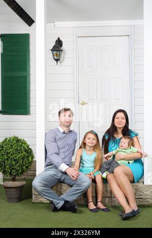 La giovane famiglia felice di quattro persone si siede sul portico del nuovo cottage. Foto Stock