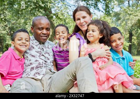 Una famiglia interrazziale di sei persone si siede sull'erba del prato nel parco Foto Stock