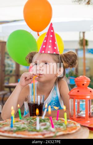 Ragazza in un berretto celebrativo in un bar che beve attraverso una paglia Foto Stock