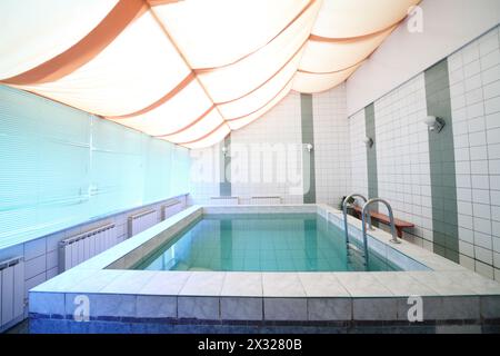 Una piccola piscina interna con piastrelle sulle pareti e sul pavimento e tende sulle finestre Foto Stock