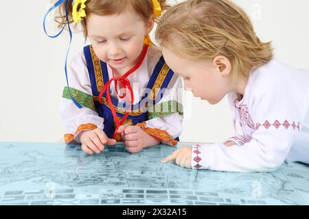 Bambino e ragazza in costumi popolari russi guardano la mappa varicolored su sfondo bianco. Foto Stock