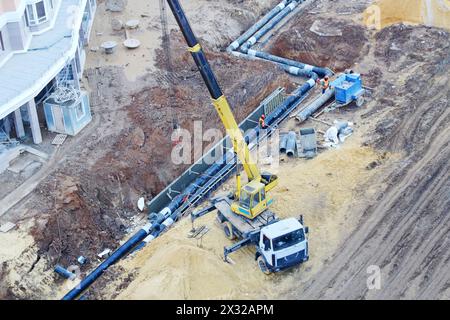 La gru per autocarri colloca tubi sotterranei in cantieri edili di grandi dimensioni. Foto Stock