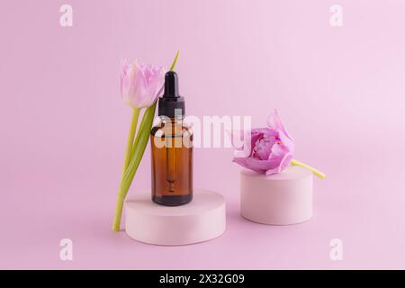 Prodotto di bellezza alla moda, siero in bottiglia cosmetica di vetro con contagocce per la cura della pelle del viso e del corpo in piedi su un podio di cemento rotondo con un fiore di tulipano Foto Stock