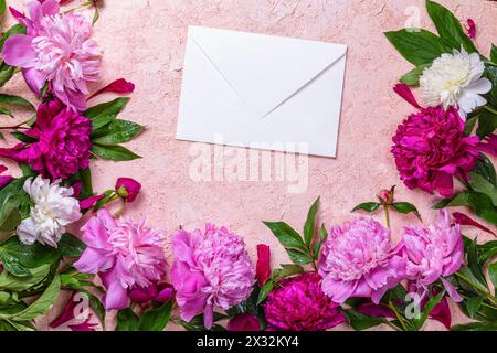 Disposizione astratta della cornice floreale con busta di carta. Peonie su sfondo rosa. Composizione romantica, piano, vista dall'alto Foto Stock