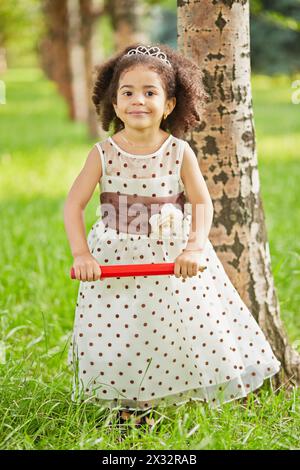 La bambina vestita con un abito a pois si trova nel parco tenendo in mano una grande matita rossa Foto Stock