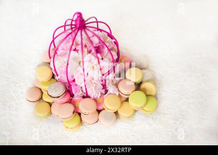 Biscotti colorati con panna sul tavolo con fiori in piccola gabbia, foto con messa a fuoco sof. Foto Stock