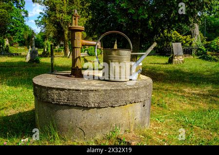 Evangelischer Friedhof Pokoj, Woiwodschaft Opole, Polen Friedhofsromantik mit zerbeulter Gießkanne auf einem Wasserbrunnen mit Handpumpe, historischer Evangelischer Friedhof Bad Carlsruhe Pokoj, Kreis Namslau Namyslow, Woiwodschaft Oppeln, Oberschlesien, Polen. Il romanticismo del cimitero con una lattina da annaffiare ammaccata su un pozzo pompato a mano, lo storico cimitero protestante di Pokoj, il distretto di Namyslow, il voivodato di Opole, l'alta Slesia, Polonia. Foto Stock