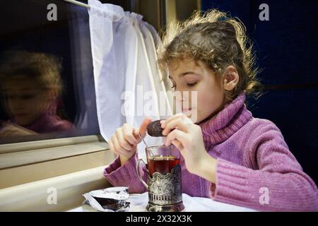 La bambina beve tè e mangia biscotti al cioccolato al tavolo nel reparto pullman Foto Stock