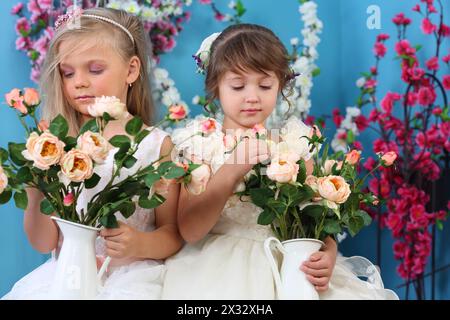 Due bambine in abiti bianchi guardano mazzi di rose in camera con fiori. Foto Stock