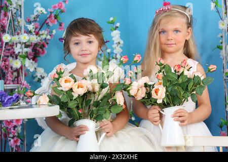 Due graziose bambine in abiti bianchi tengono rose in camera con fiori. Foto Stock