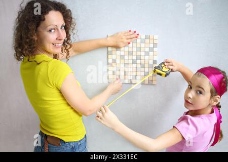 La figlia aiuta sua madre a misurare la piastrella di finitura Foto Stock