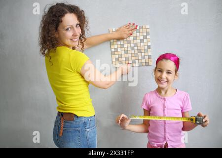 Felice figlia aiuta sua madre a misurare la piastrella di finitura Foto Stock