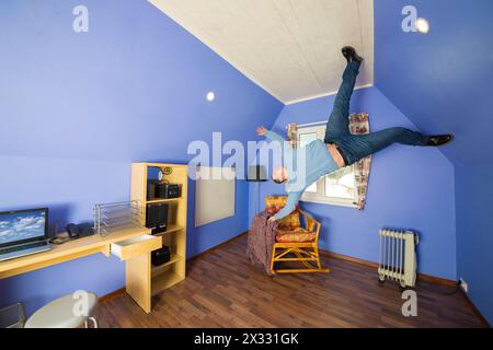 Uomo in jeans che corre sul soffitto a testa in giù a casa rovesciata Foto Stock