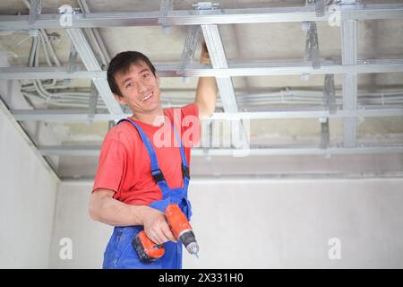 Il lavoratore sorridente sta installando un profilo a soffitto per controsoffitti Foto Stock