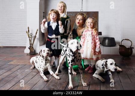 Bella donna in costume medievale con tre bambini e tre dalmati si meravigliano vicino al camino. Foto Stock