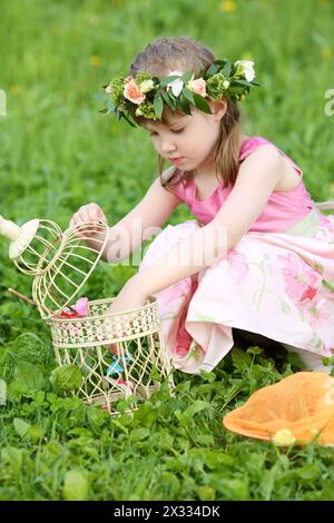 La piccola bella ragazza in rosa fa uscire le farfalle dal coop sul prato verde. Foto Stock