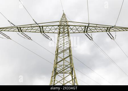 piegare la linea elettrica aerea per l'elettricità fotografata dal basso nella sezione sottostante e sui lati di fronte a un cielo grigio nuvoloso Foto Stock