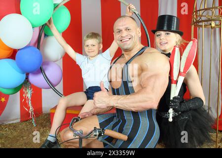 Circo felice uomo forte, donna in cilindro e ragazzo con moto retrò con palloncini in tenda a righe Foto Stock