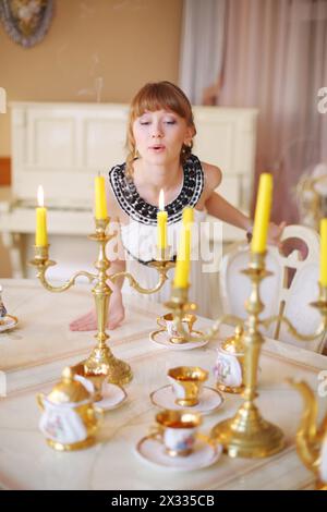 Una bella ragazza sta vicino a un tavolo bianco con piatti e fa saltare le candele. Foto Stock