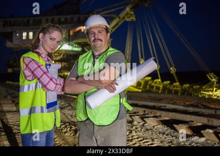 due operai si trovano sullo sfondo di un'impilatrice di carriera Foto Stock