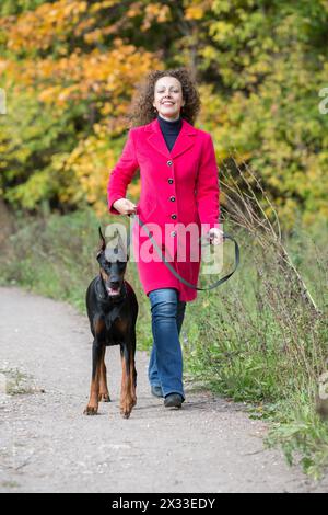 Una donna felice con un cappotto rosso cammina con il cane nero. Foto Stock