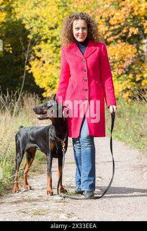 Una bella donna sta camminando con un cane nel parco autunnale. Foto Stock