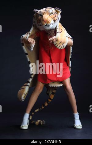 Bambina con un vestito rosso nella pelle della tigre isolata sul nero Foto Stock