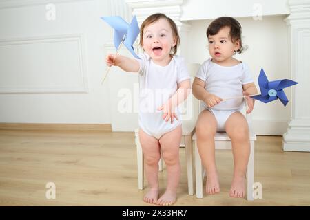 Due bambini piccoli seduti su sedie bianche con vortici di carta blu Foto Stock