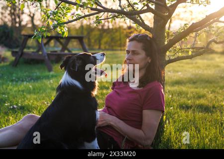 La donna si sta godendo la primavera con il suo cane nel parco. Il proprietario di animali domestici si rilassa con un collie di confine all'aperto durante il tramonto Foto Stock