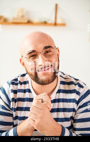Un uomo calvo con gli occhiali ha una posa premurosa a casa. Foto Stock