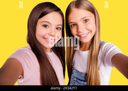 Foto ravvicinata due bambine la sua bionda bruna ragazze lunghe e graziose telefonate per capelli fanno selfie mamma skype Talk Tell Speak indossando un casual Foto Stock