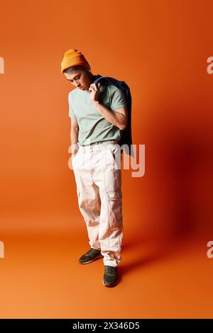 Un bell'uomo asiatico posa con sicurezza in una camicia verde e pantaloni bianchi su uno sfondo arancione in un ambiente studio. Foto Stock