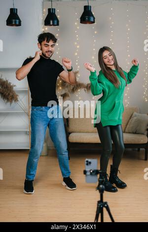 Uomo e donna che registrano video danze utilizzando lo smartphone a casa. I talenti della generazione Z giocano a selfie video app per lo show Condividi la storia virale. Foto Stock
