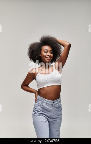 Una splendida giovane donna afroamericana con i capelli ricci posa con fiducia per una foto in un ambiente da studio. Foto Stock