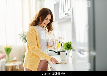 Una donna di mezza età sta tranquillamente in piedi a un bancone con una tazza di caffè. Foto Stock