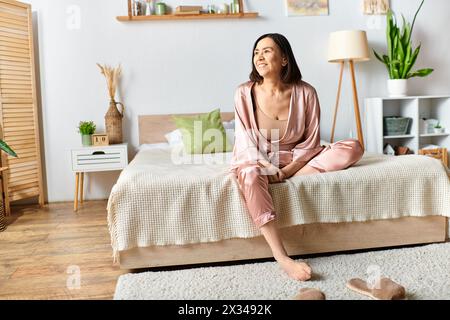 Una donna matura siede tranquillamente in cima a un letto in un'accogliente camera da letto. Foto Stock