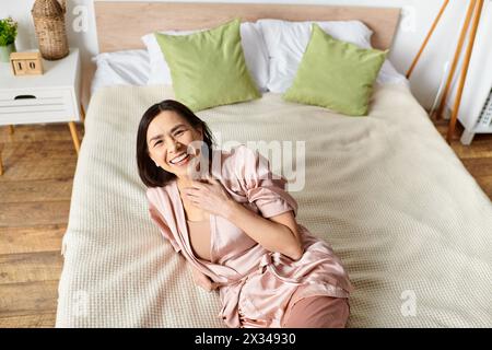 Una donna matura si rilassa sul letto rosa in un comodo accappatoio. Foto Stock