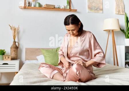 Una donna matura in pigiama rosa siede comodamente su un letto. Foto Stock