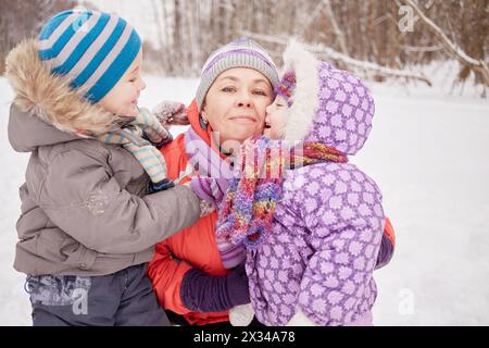 Mamma felice con due bambini nel parco invernale innevato. Foto Stock