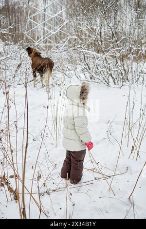 I bambini vestiti con abiti caldi guardano le alci che si nutrono nel parco invernale. Foto Stock