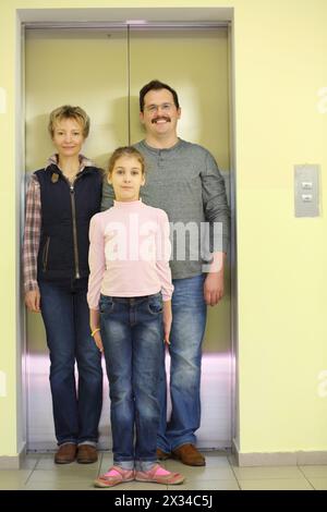 Ritratto di famiglia delle tre persone di fronte a un ascensore chiuso, concentrati sulla ragazza Foto Stock