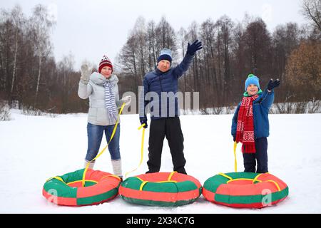 Madre, padre e figlio con i tubi di neve ondeggiano le mani in inverno, concentratevi sull'uomo Foto Stock