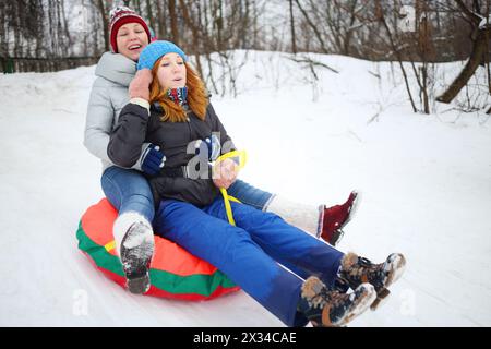 Mamma felice con una ragazza adolescente su un tubo di neve giù per la collina durante il giorno d'inverno Foto Stock