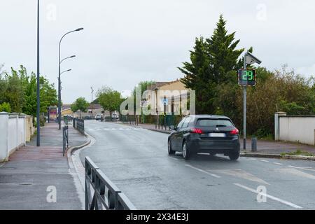 Bordeaux, Francia - 26 aprile 2023: Un'auto percorre una strada suburbana bagnata, superando un display digitale di velocità che mostra 29 chilometri all'ora, con copertura Foto Stock