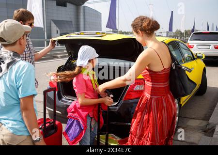 la madre con due bambini mette i bagagli nel bagagliaio del taxi, concentrandosi sull'autista Foto Stock