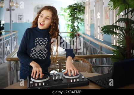 Bella ragazza felice con capelli ricci canta dietro la console del DJ nel bar Foto Stock